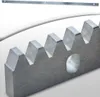 A close-up view of a metal rack with gear teeth and a hole, with a long, thin toothed metal strip in the background. Náhľad obrázku produktu