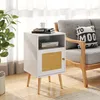 A white wooden nightstand with a rattan door is placed next to a gray sofa in a living room. Podgląd zdjęcia produktu