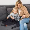 A woman is sitting on a couch with a baby on her lap, and they are looking at a soft book. Produktbild-Vorschau