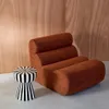 A brown upholstered chair and a black and white striped stool are placed on a concrete floor against a wood-paneled wall. Produktbild-Vorschau