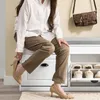 A person is sitting on a shoe bench in a hallway, putting on shoes. Produktbild-Vorschau