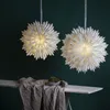 Two white paper star lanterns hang against a dark green background, with a table and draped fabric in the foreground. Podgląd zdjęcia produktu