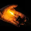 A hand holding a lit incandescent light bulb against a black background. Podgląd zdjęcia produktu