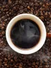 A close-up overhead view of a white mug filled with dark coffee, surrounded by roasted coffee beans. Anteprima dell’immagine prodotto