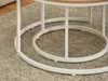 A close-up view of the white metal legs and circular base of two nesting coffee tables, resting on a patterned rug. Podgląd zdjęcia produktu