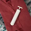 A red knitted cardigan is laid flat with a white manual vacuum pump placed on top of it. The background is a clear plastic sheet with repeating text. Anteprima dell’immagine prodotto