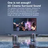 Two speakers are placed in a living room setting with a large TV in the background displaying a band playing. Produktbild-Vorschau