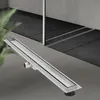 A linear shower drain is shown in the foreground, with a modern bathroom interior in the background. Náhľad obrázku produktu