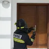 A firefighter in full gear is using a tool to open a wooden door. Produktbild-Vorschau