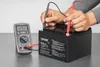 A person is testing a battery with a multimeter. Produktbild-Vorschau