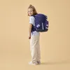 A young girl wearing a backpack and standing against a plain background. Podgląd zdjęcia produktu