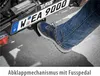 A person's foot is pressing on a pedal of a bicycle rack attached to a vehicle. Produktbild-Vorschau