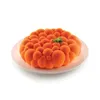 A round, orange cake with a textured, bubbly surface, decorated with a small sprig of mint, sits on a white plate against a white background. Anteprima dell’immagine prodotto