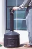 A person is using a black outdoor ashtray stand next to a building entrance. Voir les images du produit