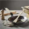 A de Buyer Mineral B frying pan and wooden kitchen utensils are arranged on a textured surface, with a wooden pepper mill and a piece of wood in the background. Anteprima dell’immagine prodotto