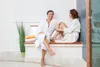 A couple in bathrobes relaxing on a bench in a spa. Produktbild-Vorschau
