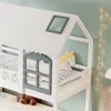 A close-up view of a white house-shaped bunk bed with a gray window and a yellow horse pillow. Produktbild-Vorschau