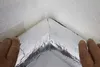 Hands are shown applying reflective insulation material to an interior corner of a room. Produktbild-Vorschau
