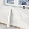 A roll of clear protective film is shown leaning against a white wall next to a window. Produktbild-Vorschau