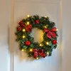 A Christmas wreath decorated with red bows, red baubles, and LED lights, hanging on a white door. Produktbild-Vorschau