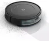 A black, round robot vacuum cleaner is shown on a white surface, with dust particles scattered around it. Podgląd zdjęcia produktu