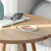 A smartphone is charging on a small wooden table next to a book and a vase. Produktbild-Vorschau