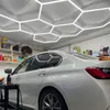 A white car is being detailed in a workshop with hexagonal lights on the ceiling. Podgląd zdjęcia produktu