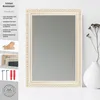 A decorative mirror with a white and gold ornate frame is displayed on a white surface, next to a white vase with dried flowers. Produktbild-Vorschau