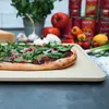 A pizza stone with a pizza on it, surrounded by ingredients like tomatoes, garlic, and herbs. Náhled obrázku produktu