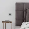 A wall socket is shown on a white wall next to a bed with a grey headboard. Produktbild-Vorschau