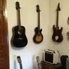 Several guitars are mounted on a wall, with a small amplifier on a wooden table below. Voir les images du produit