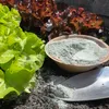 A close-up shot of lettuce plants in a garden bed, with a bowl of fine gray powder and a garden trowel filled with the same powder. Produktbild-Vorschau