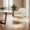 A cream-colored swivel chair with gold legs is placed in a well-lit room with a marble-top dining table and a large window in the background. Voir les images du produit