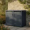 A dark gray bin storage unit for two trash cans is shown outdoors against a brick wall, with plants and paving stones. Produktbild-Vorschau