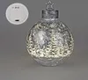 A decorative Christmas ornament with a winter forest scene illuminated by LED lights, shown against a plain gray background. A separate image of the battery compartment is visible in the upper left corner. Produktbild-Vorschau