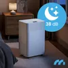A white dehumidifier is placed on a carpeted floor next to a wooden nightstand with a lamp. A blue overlay with a moon and stars and text "38 dB" is in the upper right corner. A logo is in the bottom right corner. Voir les images du produit