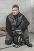 A construction worker kneels on the floor of a building under construction, holding a coiled extension cord. Podgląd zdjęcia produktu