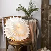 A white paper star lantern is placed on a wooden chair next to a table with a vase of greenery. Podgląd zdjęcia produktu