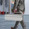 A person in a grey jumpsuit is carrying a silver toolbox in a garage setting. Podgląd zdjęcia produktu