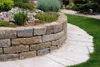 A curved stone wall and pathway in a garden setting. Produktbild-Vorschau
