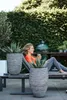 A woman relaxing on a lounge chair outdoors with two large planters in the foreground. Voir les images du produit
