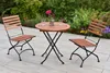 A wooden folding table and two chairs set up on a patio with a garden in the background. Produktbild-Vorschau