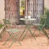 A bistro set with a round table and two chairs on a brick patio in front of large wooden doors. Produktbild-Vorschau