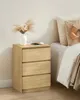 A bedside table with a vase of dried flowers and a phone charging next to a bed. Náhled obrázku produktu