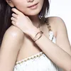 A close-up shot of a woman wearing a silver and gold watch on her wrist, with a white dress and gold chain detail visible. Produktbild-Vorschau