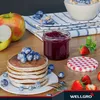 A breakfast scene with pancakes, jam, fruit, and a bowl of cereal. Produktbild-Vorschau
