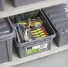 Fishing lures are stored in a gray plastic storage box on a shelf. Anteprima dell’immagine prodotto
