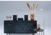 A stereo system is displayed on a black cabinet with decorative geometric patterns. There are also champagne glasses, a vase with dried flowers, and a floor lamp. Anteprima dell’immagine prodotto