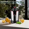 A stainless steel citrus juicer is displayed on a white surface with lemons and a glass of juice, with greenery in the background. Produktbild-Vorschau