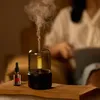 An aroma diffuser and essential oil bottle are placed on a wooden tray, with a person blurred in the background. Podgląd zdjęcia produktu